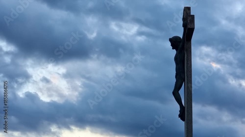 Stone statue representing Jesus Christ crucifixion, at sunset, 4K clouds time lapse