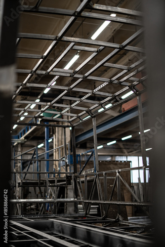 Industrial vehicle manufacturing workshop with metal bus frames and body structures under assembly. Large factory interior shows fabrication, welding, and custom vehicle production in progress.