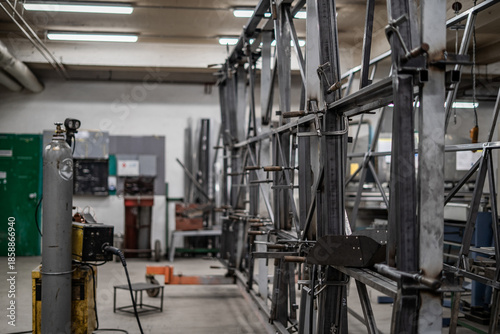 Industrial vehicle manufacturing workshop with metal bus frames and body structures under assembly. Large factory interior shows fabrication, welding, and custom vehicle production in progress.