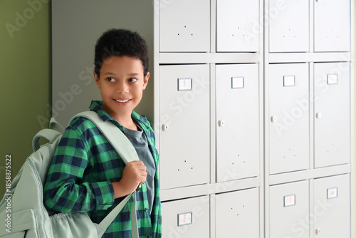 Teenage African-American schoolboy with backpack near locker on green background