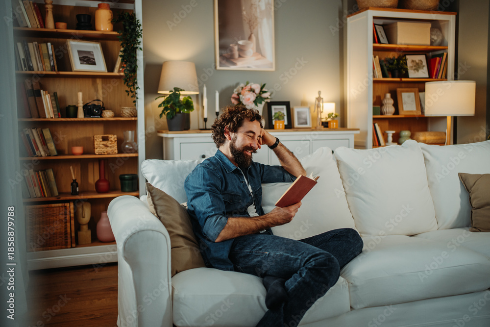 Obraz premium Happy man relaxing on sofa reading book at home