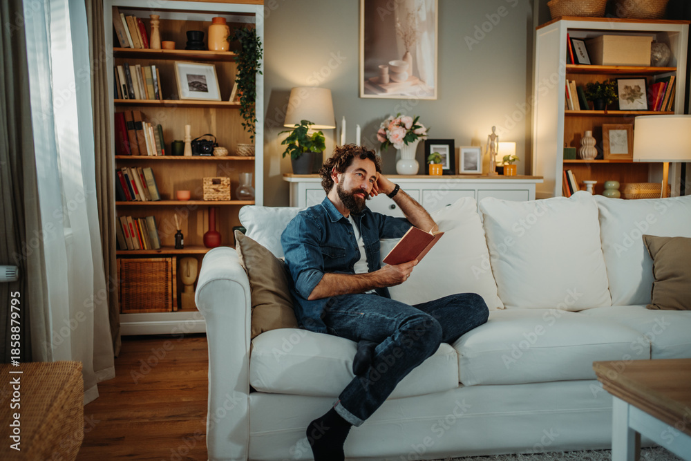 Obraz premium Thoughtful man relaxing reading book on sofa at home library
