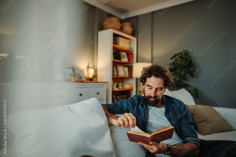 Fototapeta premium Man relaxing on sofa reading book at home