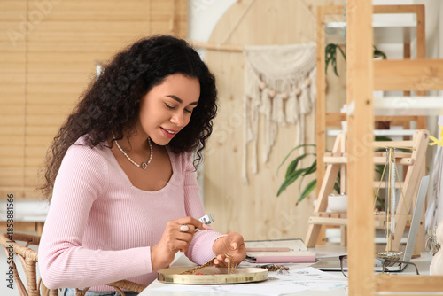 Tableau sur toile Happy young African-American female jewelry designer examining necklace with mag