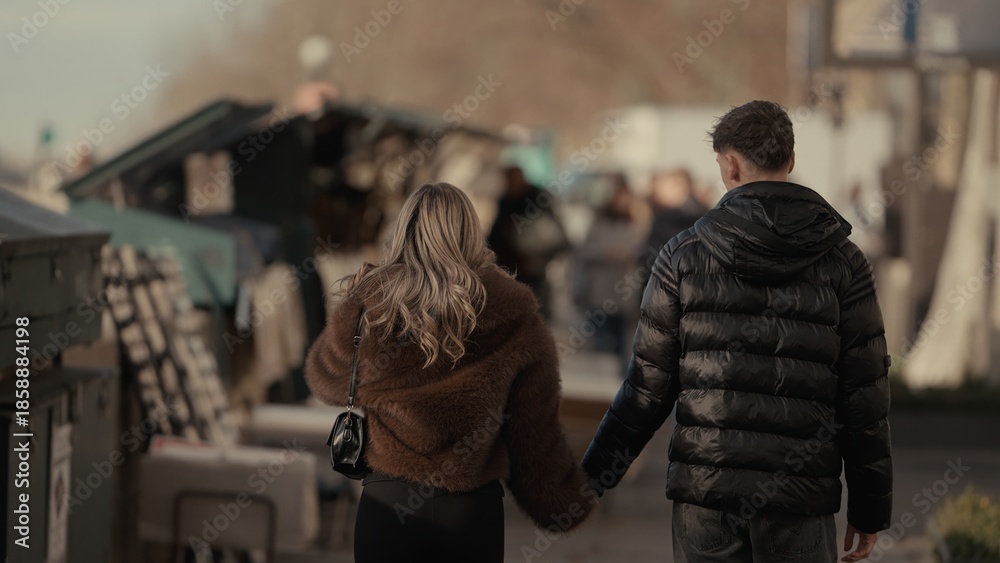 Fototapeta premium A romantic couple is holding hands while walking along the Seine River in Paris France. This image can be used commercially for travel romance and European city themes.