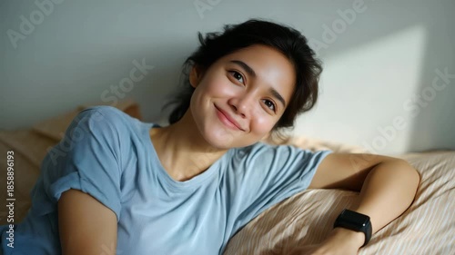young Asian woman in her early 20s is shown lying on her side in bed, captured from the chest up, fully in frame with enough headroom and negative space to avoid any cropping. She