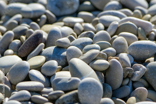 A close up of smooth light and dark gray stones and rounded pebbles forming a natural pattern on the beach ground under bright sunlight