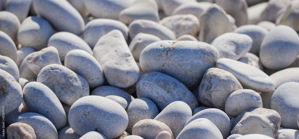 Fototapeta premium A close up view of light gray white rounded pebbles and stones covering a natural Mediterranean beach on a sunny day perfect for a summer holiday background