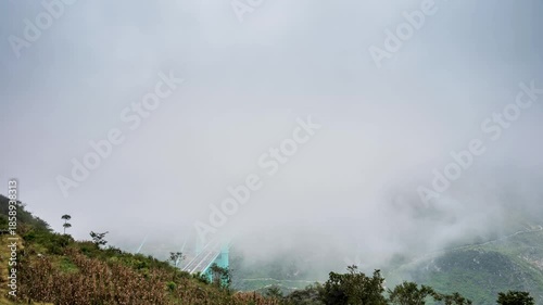 time-lapse of the Huajiang Canyon Bridge in Guizhou, China, emerging from thick mist over a deep canyon. Dramatic clouds swirl around the modern suspension bridge.
