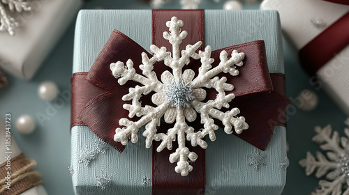 Wrapped gift box with white snowflake ornament and dark red ribbon bow.