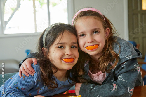 Funny portrait of two little girls posing for a photograph with big orange fruit smiles