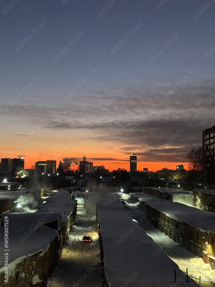 Fototapeta premium The silhouette of the city at sunset. The shadows of the houses, the warm light of the sun over the horizon. Novosibirsk 2025
