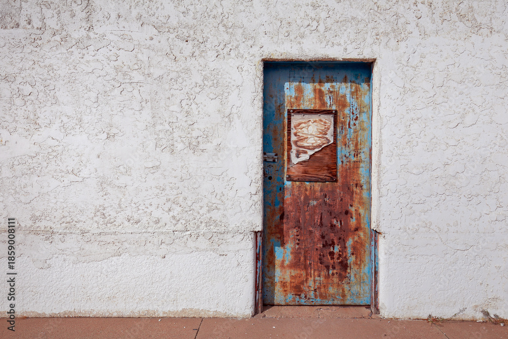 Fototapeta premium Old rusted metal door in a stucco wall in the western USA
