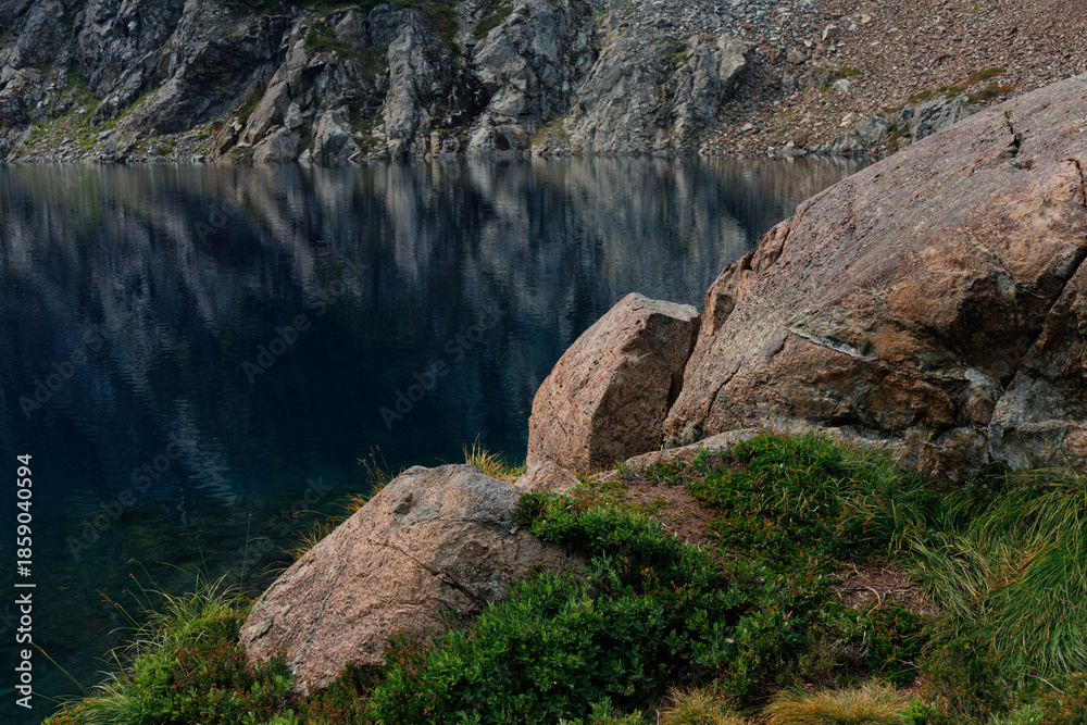 Obraz premium Rocks covered with grass are located on the shore of a mountain lake.