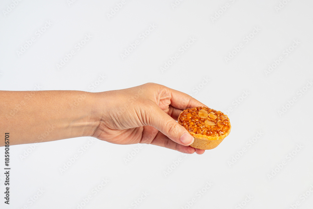 Fototapeta premium An almond and nut cupcake topped with a small amount of caramel is held in a hand against a white background.