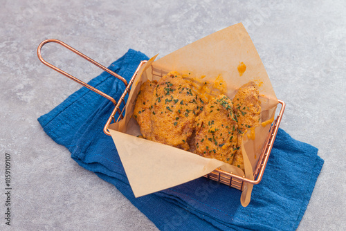 A basket of golden fried chicken pieces coated with herb seasoning, served on parchment paper over a blue cloth for a stylish look.