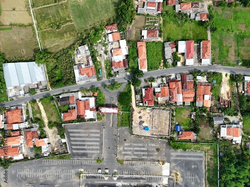 Aerial view of small rural village with houses, roads, parking area, and surrounding green fields