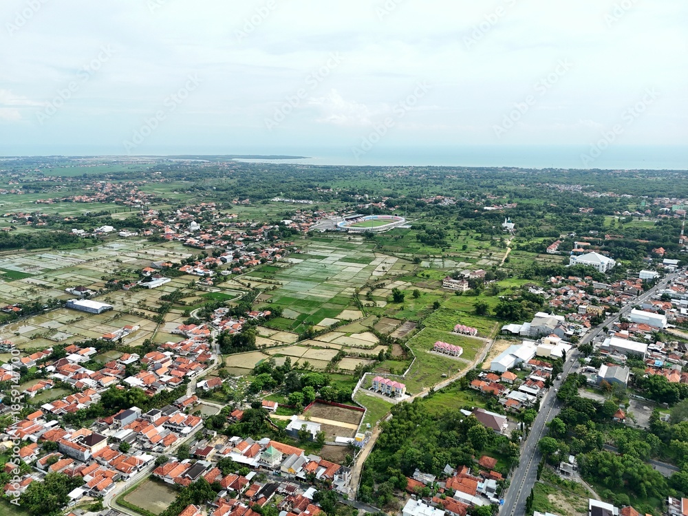 Fototapeta premium Wide aerial view of suburban town with red roof houses blending into green farmland landscape