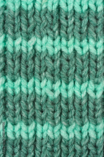 A close up macro shot of a green hand knitted woolen fabric with alternating horizontal stripes in different shades of green