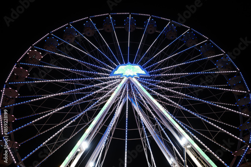 Low-angle night photograph of a large illuminated Ferris wheel against a deep black sky.