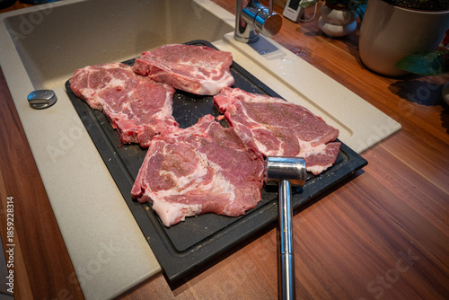 High-quality kitchen scene featuring four raw pork steaks seasoned with salt and pepper, arranged on a black cutting board next to a sink