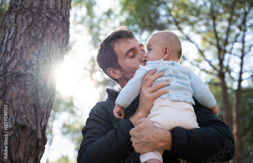 Father kissing baby outdoors with natural sunlight in nature