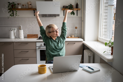 Satisfied middle aged businesswoman warming up body after successfully finishing work tasks and projects on laptop. Cheerful female worker stretching arms muscles, taking break from work on computer.