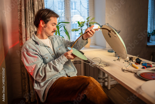 Upcycling master renovating old vintage lamp at home workshop, sitting at worktable checking assembled item, holding and evaluating conditions of bottom base part and wiring system, refurbishing hobby