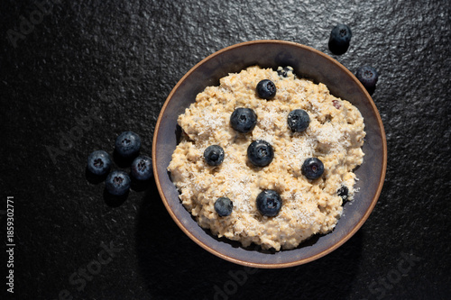 Porridge mit Blaubeeren und Kokosraspel auf dunklem Hintergrund. Granitplatte. Foodphotography