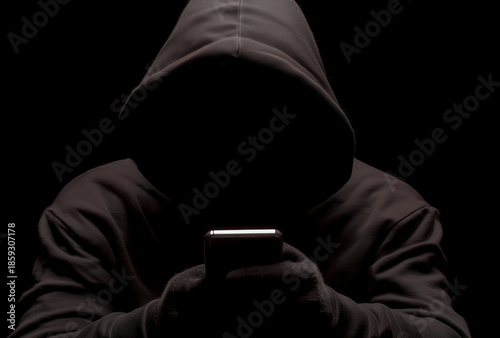  a hacker in a black hoodie holding a mobile phone