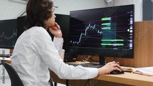 Real time monitoring graphs are on the screens. Young man is sitting in the office with multiple displays of stock market data