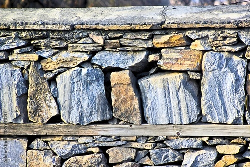 A close-up view of a wall constructed from stacked rocks and capped with concrete.
