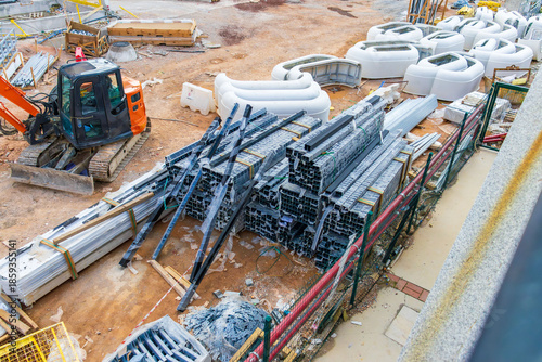 Construction site with excavator and stacks of metal beams and building materials.