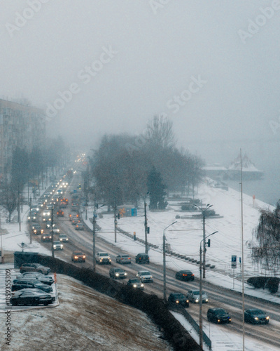 City traffic in extreme winter conditions: cars on a multi-lane road in thick snow and fog. The photo showcases winter logistics, everyday city life in inclement weather, and the atmosphere of a cold,