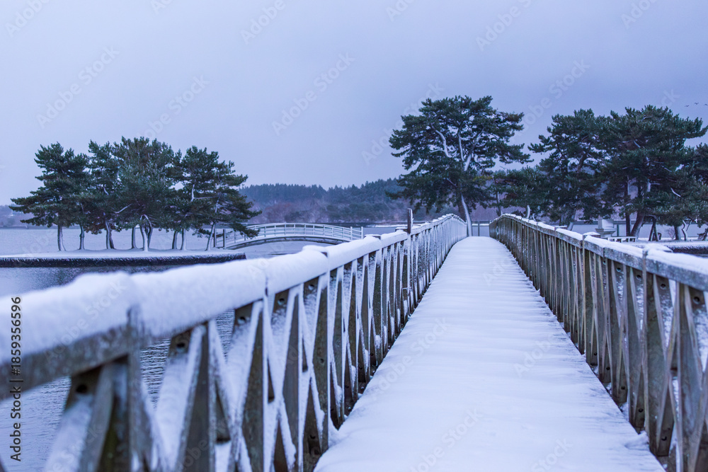 Obraz premium Snow-covered wooden footbridge in a winter landscape in Japan.