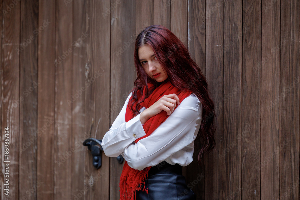 Fototapeta premium Young woman posing in front of wooden door with red scarf