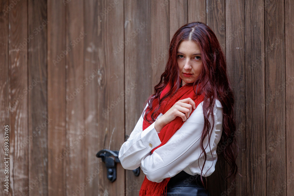 Fototapeta premium Young woman posing in front of wooden door with red scarf
