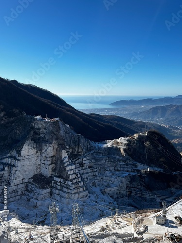 Carrara marble quarry overlooking the Mediterranean Sea, Apuan Alps, Italy, dramatic white stone excavation terraces with cables, machinery and coastal landscape under clear blue sky, Forte dei Marmi