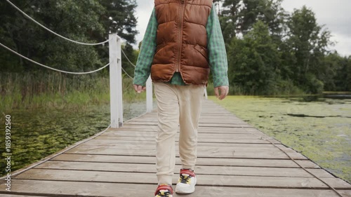 Front view of child walking confidently on wooden pier. Symbolizes growing up, independence and emotional development. High quality 4k footage
