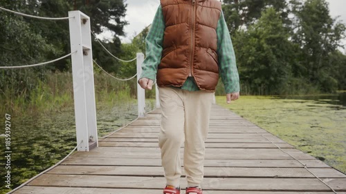A child in vest and shirt walks slowly on wooden pier. The frame highlights harmony of childhood, outdoor activity and healthy living. High quality 4k footage
