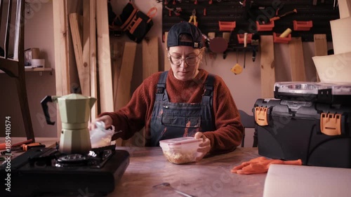 Female carpenter sitting at wooden workbench having lunch break in workshop