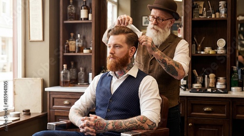 Senior barber with white beard styling hair of a tattooed young man with red beard in a vintage barbershop