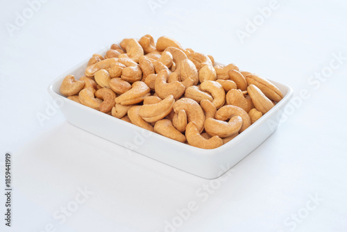 Premium grade, whole roasted cashew nuts in a white ceramic bowl on a white table.
