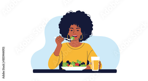 Young woman with curly hair enjoys eating a healthy green salad with vegetables and a glass of juice at a table.