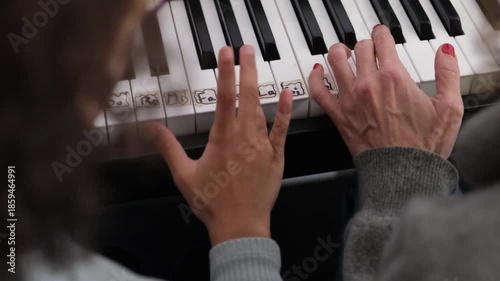 Close-up of a child's hands learning to play the piano with a teacher's guidance. The instructor helps the student find the correct keys