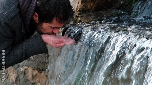 Man scooping fresh spring water from a small waterfall with cupped hands, quenching thirst in nature — pure, hydrating, refreshing moment highlighting wellness and conservation