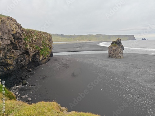 Dramatic black sand beach in Iceland with basalt cliffs and sea stacks. Stunning volcanic landscape of Reynisfjara coast under a moody sky. Scenic Nordic nature.