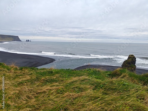 Dramatic black sand beach in Iceland with basalt cliffs and sea stacks. Stunning volcanic landscape of Reynisfjara coast under a moody sky. Scenic Nordic nature.