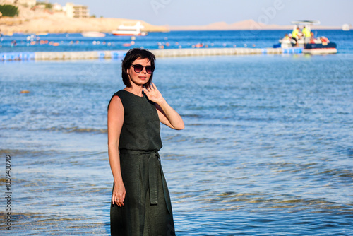 A grown woman casual clothes stands knee-deep in ocean water.