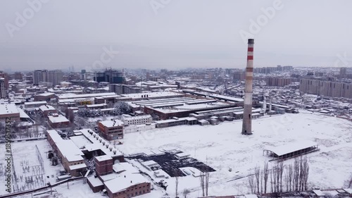 Aerial view of an aluminum factory with a large smoke stack during a snowy winter